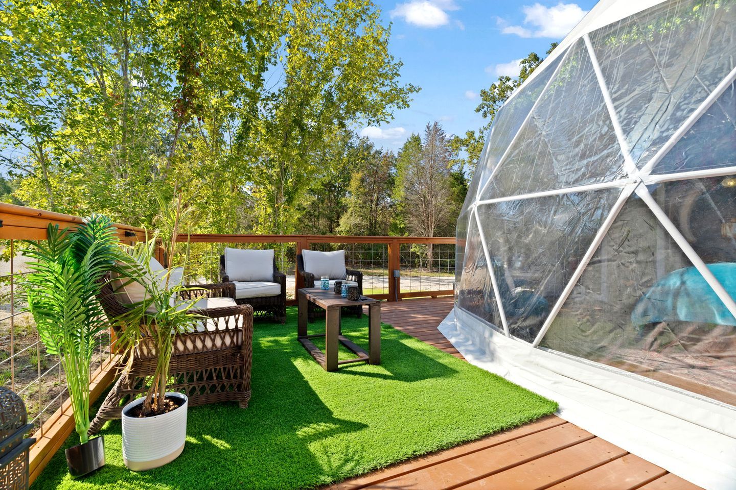 Een overdekt terras met een pergola, kunstgras en potplanten.