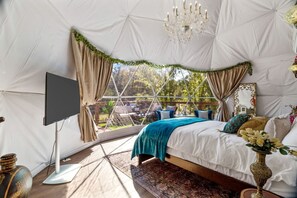 Una habitació tipus tenda amb un llit, cortines, un penjador i una televisió.