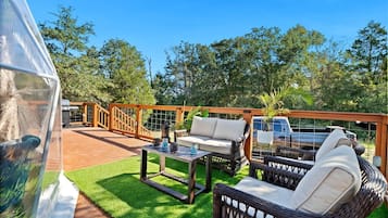 A covered outdoor area with a wooden deck, a wicker sofa, a table with candles, and a vehicle in the background.