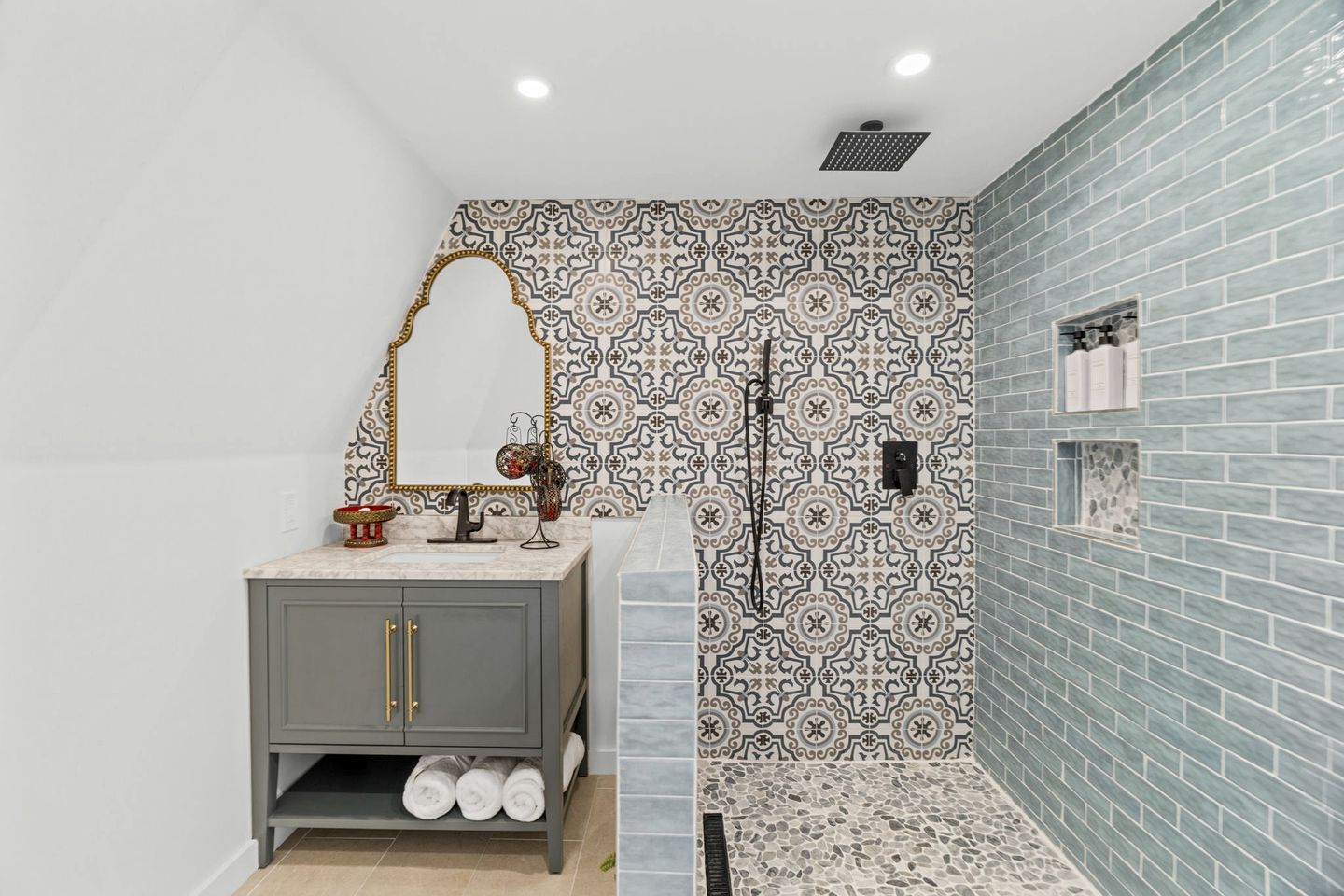 A bathroom with a gray vanity, a patterned backsplash, and a shower area with a blue-tiled wall.