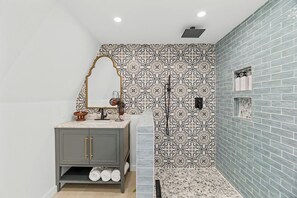 Uma casa de banho com toucador cinzento, painel de parede com padrão e área de duche com parede em azulejos azuis.