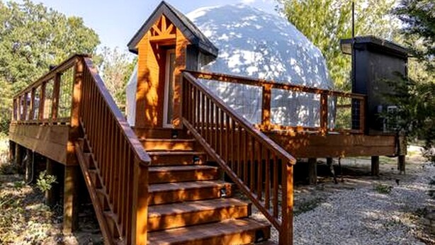 A wooden structure with a staircase leading to a dome-shaped building. - Beautiful Lofted Dome with Cozy Deck and Charming Design in Elgin, Texas (Elgin)