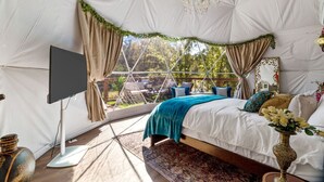 A tent-style room with a bed, curtains, a chandelier, and a TV. - Beautiful Lofted Dome with Cozy Deck and Charming Design in Elgin, Texas (Elgin)