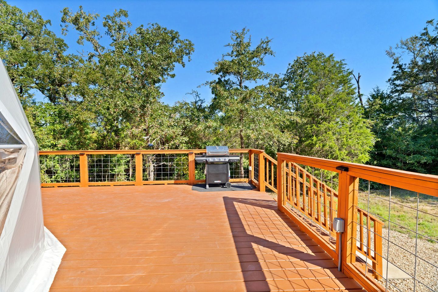 Una terraza techada al aire libre con una parrilla, rodeada de árboles.