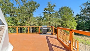 Eine überdachte Holzterrasse mit Grill, umgeben von Bäumen.
