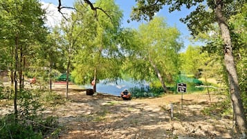 Een camping met een bord dat zwemmen in de vijver verbiedt, omringd door bomen en een heldere lucht.