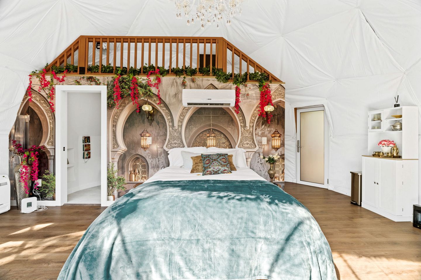 Une pièce aménagée comme une tente, avec un lit, une rambarde en bois et des arcades.