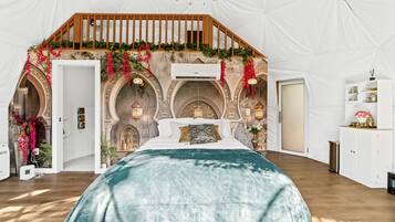 Ein Zeltraum mit Bett, Holzgeländer und Bögen.