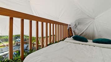 Quarto com tenda, uma cama, um ventilador e vista para o verde lá fora.
