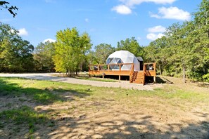 Una tenda amb forma de cúpula, amb un terra de fusta i unes escales que hi condueixen, envoltada d'arbres.