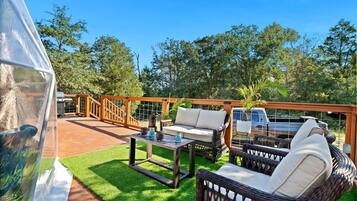 A covered outdoor area with a wooden deck, a wicker sofa, a table with candles, and a vehicle in the background.
