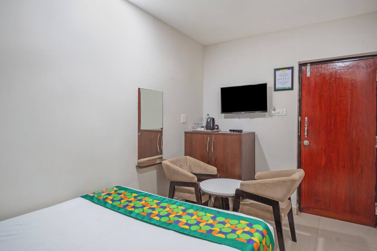 Une chambre d’hôtel avec un lit, une petite table, deux chaises, une télévision, une armoire en bois et une porte.