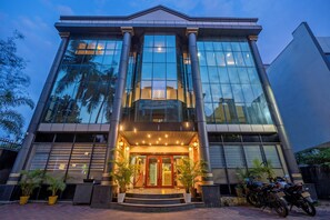 Un edificio moderno con un gran frente de vidrio, una entrada central con escalones y plantas en macetas.
