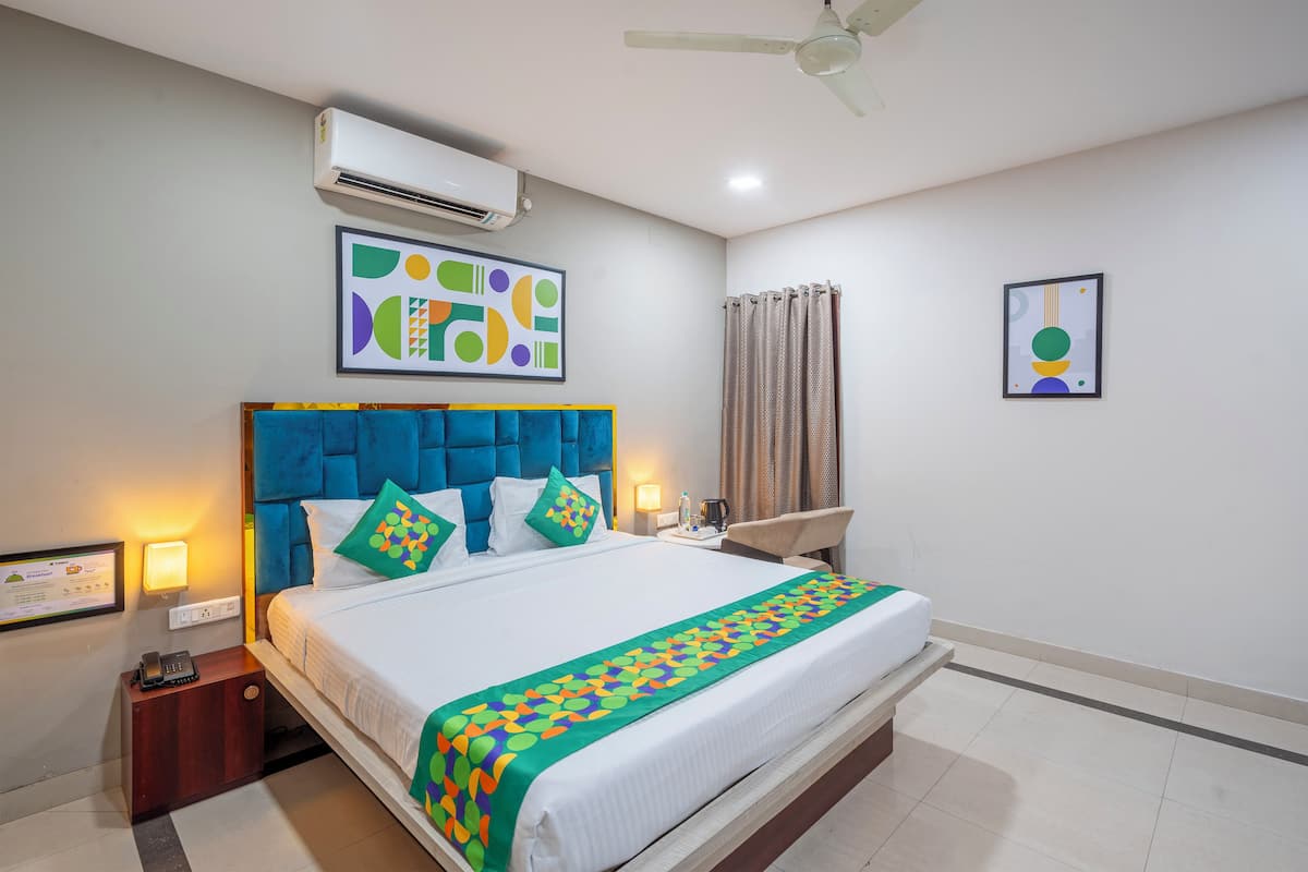 Une chambre d’hôtel comprenant un lit, une table de chevet, un climatiseur fixé au mur, un ventilateur de plafond et des œuvres d’art accrochées aux murs.