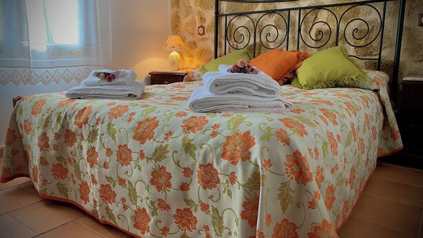 Een net opgemaakt bed met bloemenbedrukking, een lamp en een stenen muur.