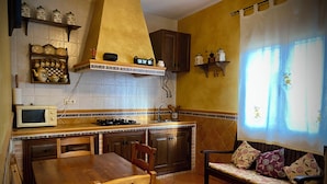 Een keuken met een eettafel, stoelen, een magnetron, een fornuis en een raam met gordijnen.