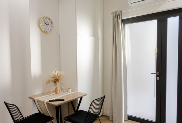 A room with a wooden table, two black chairs, a clock on the wall, and a door with curtains.