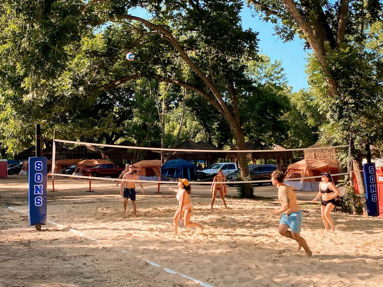 Un match de volleyball de plage avec des tentes et des voitures en arrière-plan.