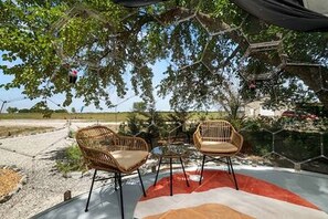 Un espace extérieur aménagé avec deux fauteuils en osier et une table, entouré d’arbres et sous un ciel dégagé.