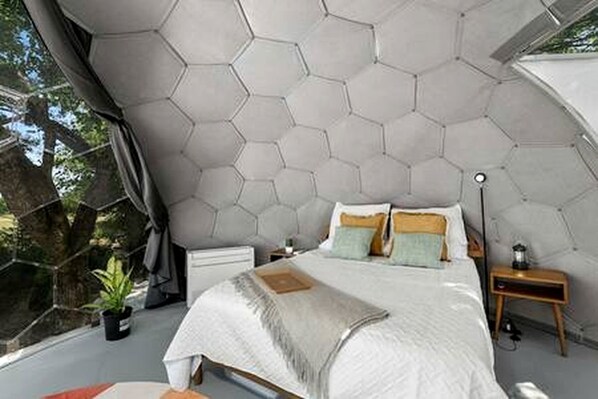 Une chambre à coucher avec un plafond hexagonal, un lit avec des oreillers, une table de chevet avec une lampe et une fenêtre avec des rideaux.