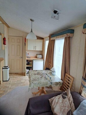 A compact living space with a kitchenette, a dining table, and a sofa. - Lyons Sunnysands Holiday Park - Holiday Accommodation 20099 (Talybont)