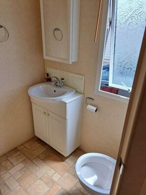 A small bathroom with a sink, toilet, and window. - Lyons Sunnysands Holiday Park - Holiday Accommodation 20099 (Talybont)