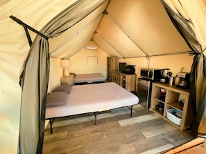 A tent with a bed, a kitchenette, and a small table.