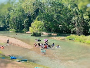 A riverbank with people engaging in various activities, including swimming and sitting on chairs.