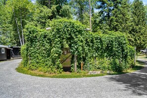 A gravel driveway leading to a gated area with a wooden structure and dense greenery.