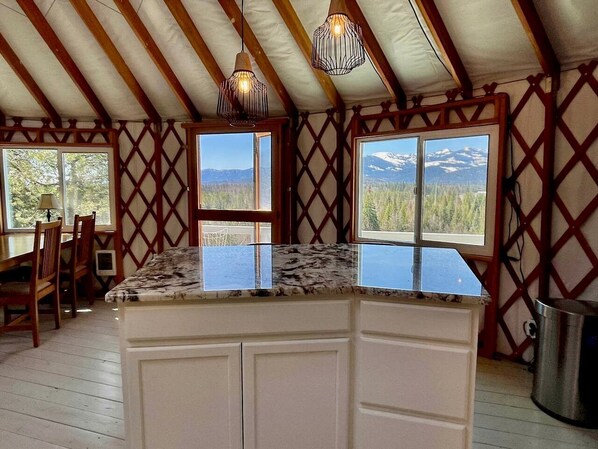 Una cocina con encimera de mármol, armarios de madera y vistas a montañas a través de amplias ventanas.