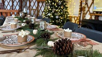 A festive indoor setting with a Christmas tree, a long dining table set with plates, candles, and pine cones.