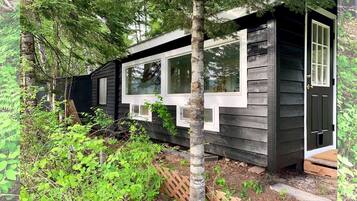 A cabin with a windowed front, surrounded by dense greenery.