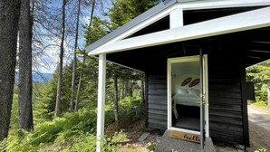 A small wooden cabin with a porch, surrounded by dense forest. - Cozy Mountain Yurt with Panoramic Views near Selkirk Mountains, Sandpoint Idaho (Sandpoint)