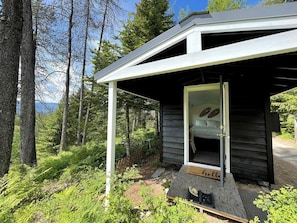 A small wooden cabin with a porch, surrounded by dense forest. - Cozy Mountain Yurt with Panoramic Views near Selkirk Mountains, Sandpoint Idaho (Sandpoint)