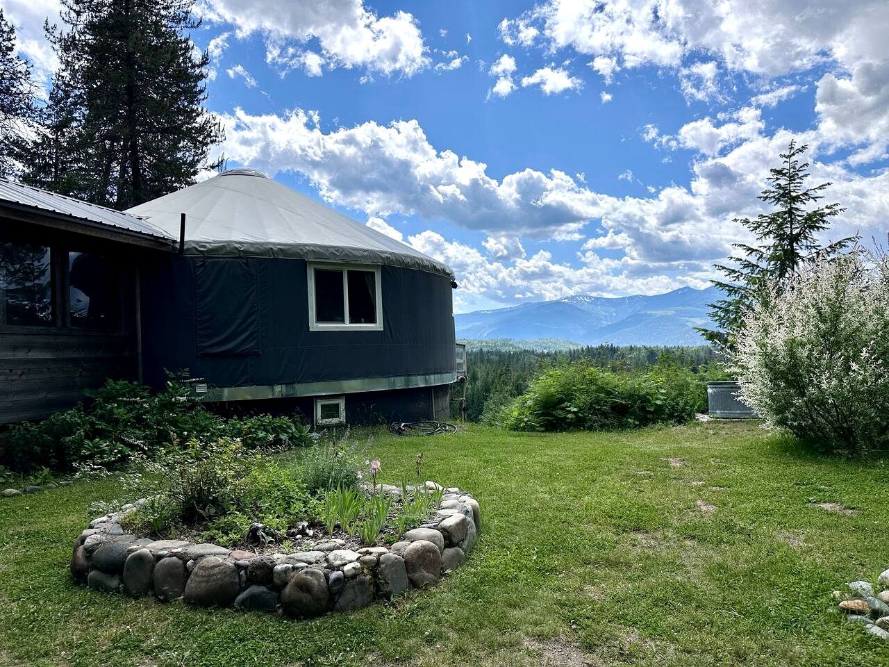 A yurt with a stone fire pit, surrounded by a grassy area and trees.