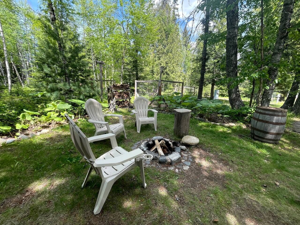A backyard with a fire pit, white Adirondack chairs, and a wooden barrel.