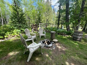 A backyard with a fire pit, white Adirondack chairs, and a wooden barrel.
