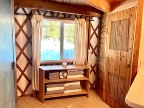 A cozy room with a wooden bench, a window with curtains, and a door with a wooden panel design. - Cozy Mountain Yurt with Panoramic Views near Selkirk Mountains, Sandpoint Idaho (Sandpoint)