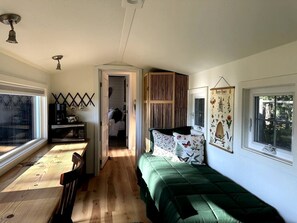 Een kleine kamer met een bed, een kitchenette, een raam en een deur naar een andere kamer.