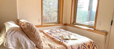 Un dormitorio con una cama, dos ventanas y vistas a árboles.