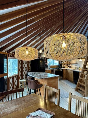 Een landelijke keuken met houten balken, een eetgedeelte met een houten tafel en twee geweven hanglampen.