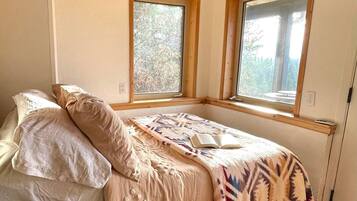 A bedroom with a bed, two windows, and a view of trees.