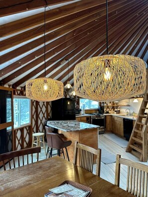 Een landelijke keuken met houten balken, een eetgedeelte met een houten tafel en twee geweven hanglampen.