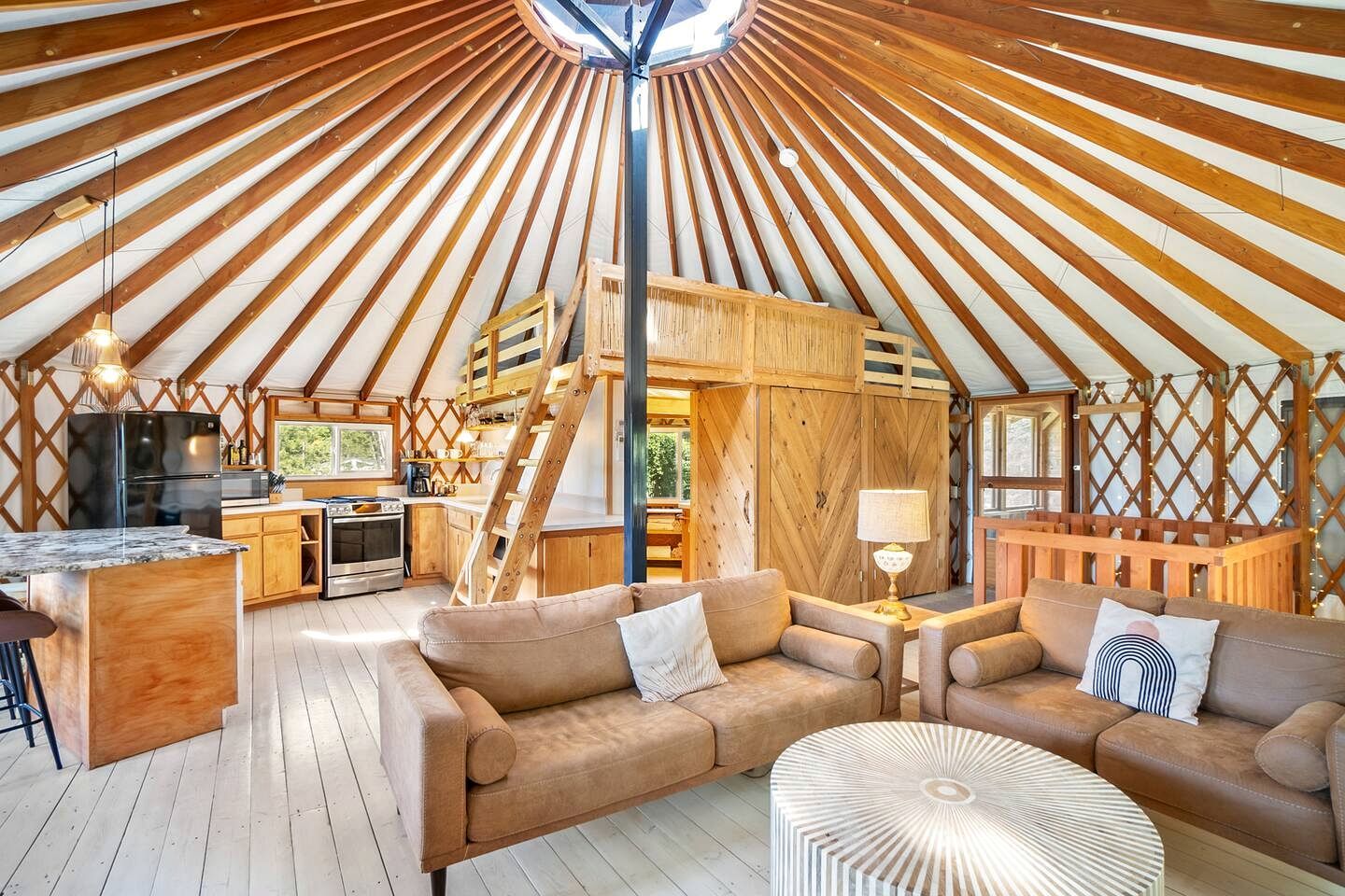 A spacious interior with a central wooden structure, a kitchen area, and seating arrangements.