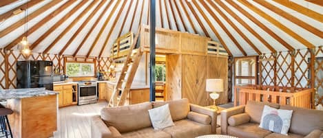 Un interior espacioso con una estructura central de madera, una zona de cocina y arreglos de asientos.