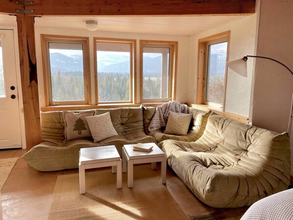 A cozy living room with a sectional sofa, two side tables, and large windows offering a mountain view.
