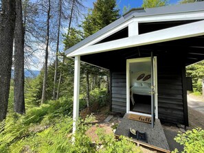 A small wooden cabin with a porch, surrounded by dense forest.