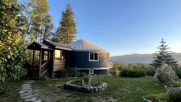 A yurt-style structure with a wooden porch, surrounded by a stone pathway and a garden.