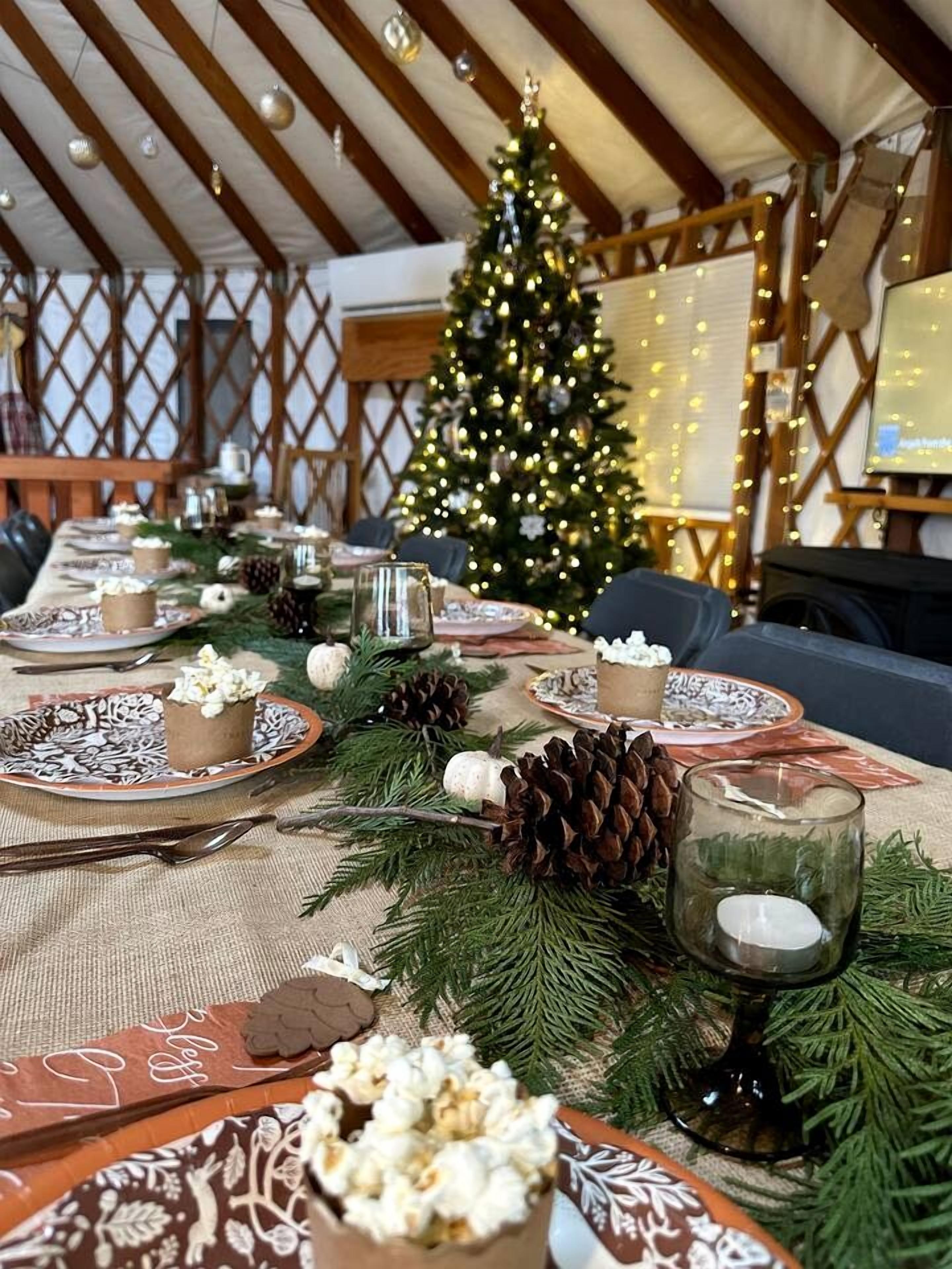 Un ambiente festivo en interiores con un árbol de Navidad, una larga mesa de comedor dispuesta con platos, velas y piñas.