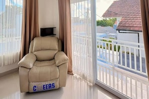Ein beiger Liegestuhl mit 'CEERS'-Branding, ein weißer Heizkörper und ein Balkon mit weißer Brüstung und Blick auf Häuser.